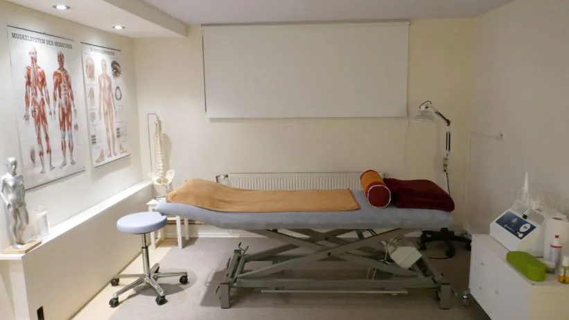 Behandlungsraum in der Naturheilpraxis mit Liege, Wärmelampe und anatomischen Lehrtafeln